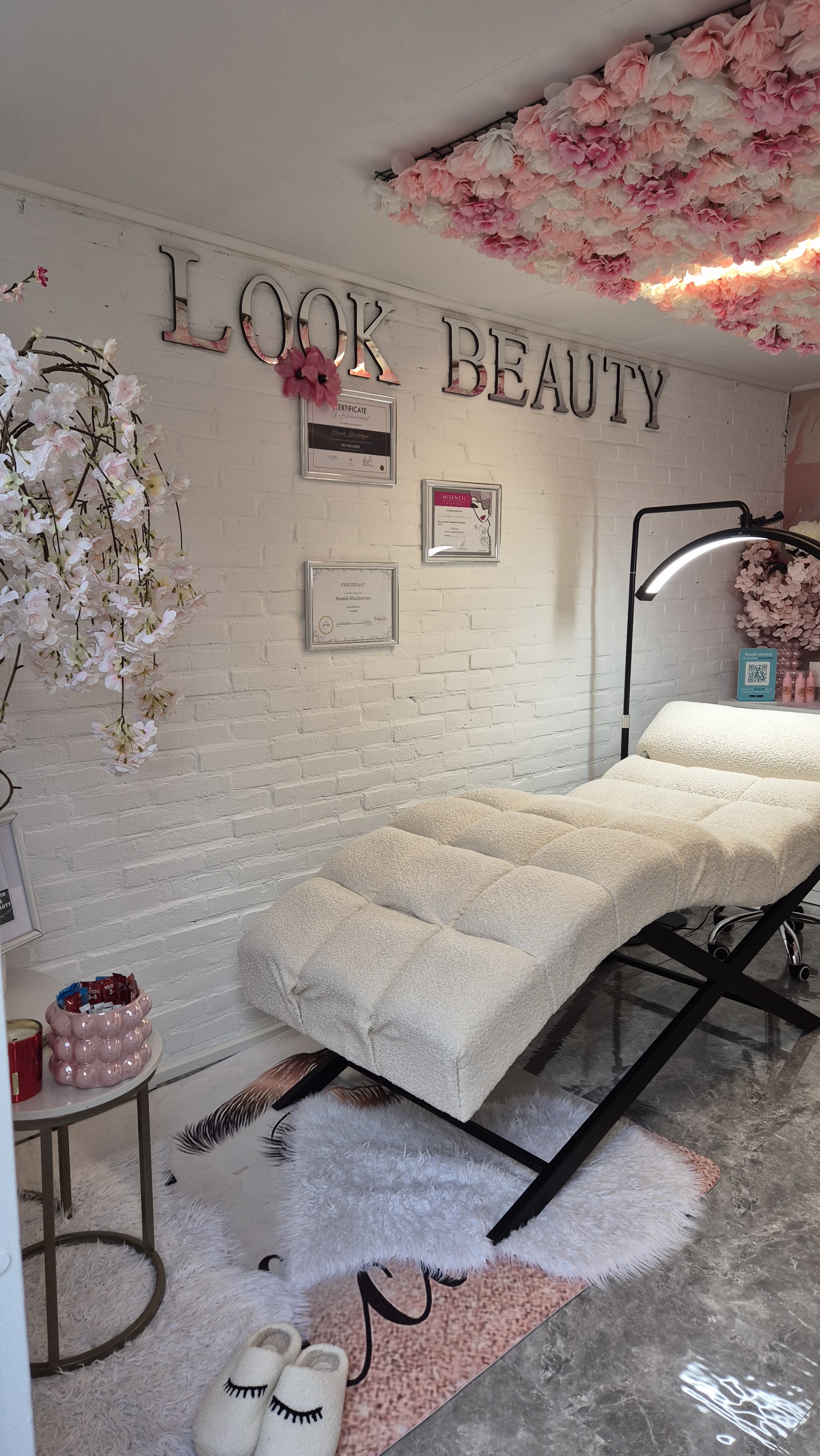 De behandelruimte met wit behandelbed, de muurletters LOOK BEAUTY en een plafond van bloemen